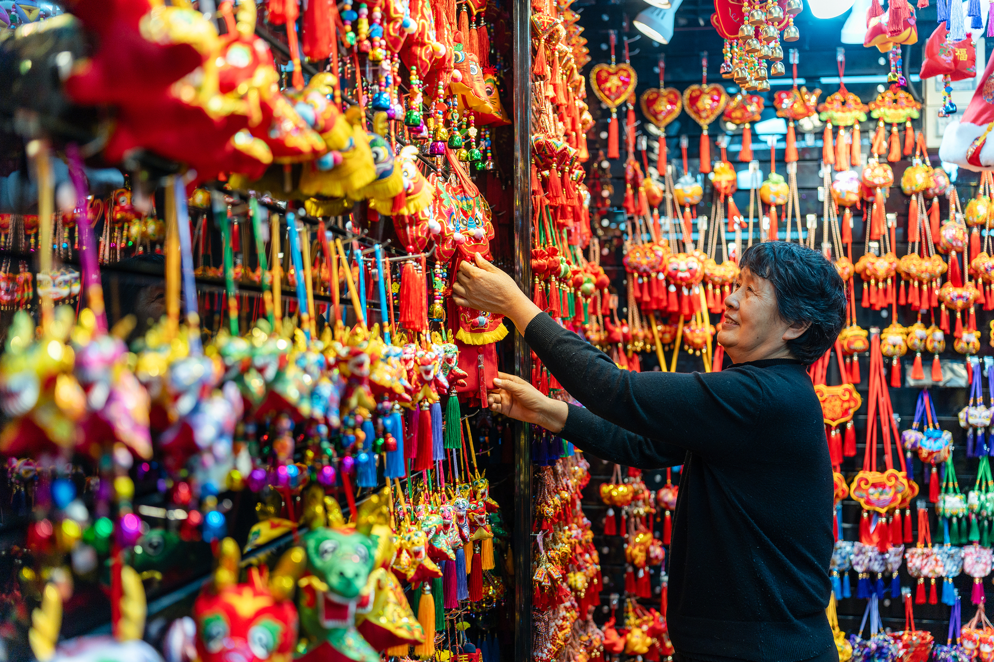 2023年12月11日，金華義烏國(guó)際商貿(mào)城，龍年喜慶用品掛滿(mǎn)攤位，顧客正在挑選中。